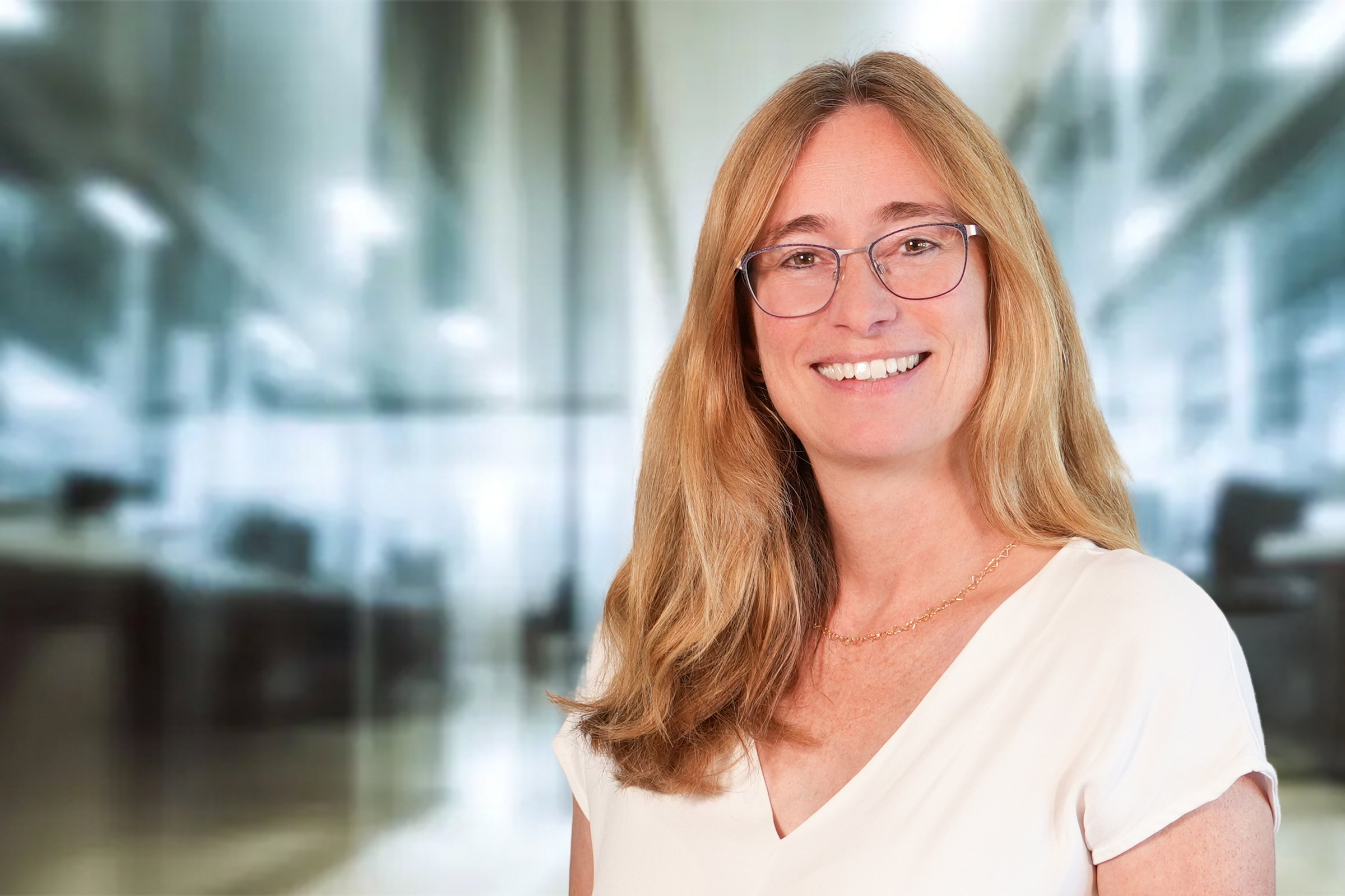Julia Sessler, Frau mit langen, mittelblonden Haaren und Brille im cremefarbenen Kurzarmshirt mit V-Ausschnitt