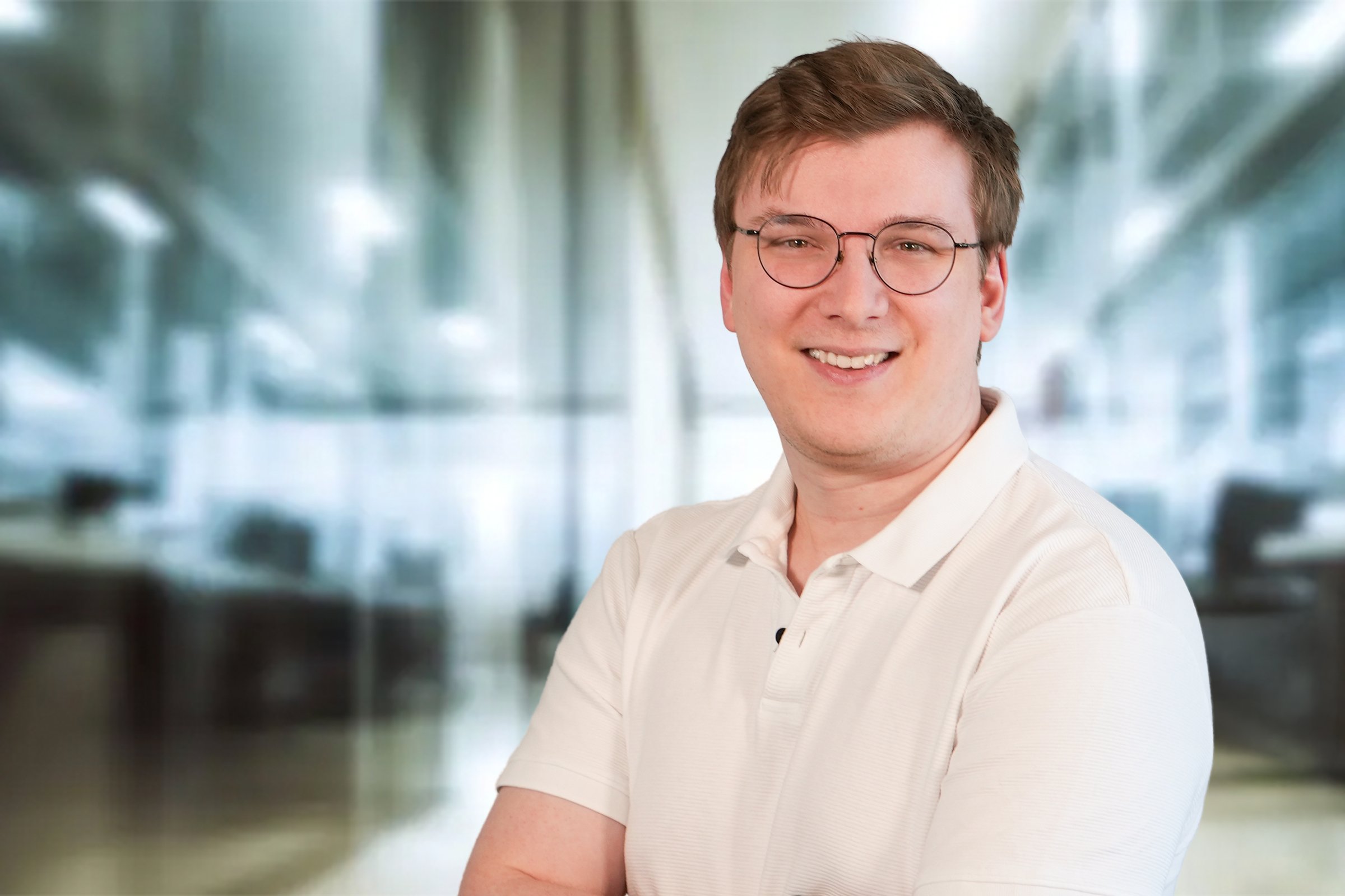 Max Dannenmann, junger Mann mit mittelblonden, kurzen Haaren und Brille mit cremefarbenen Poloshirt