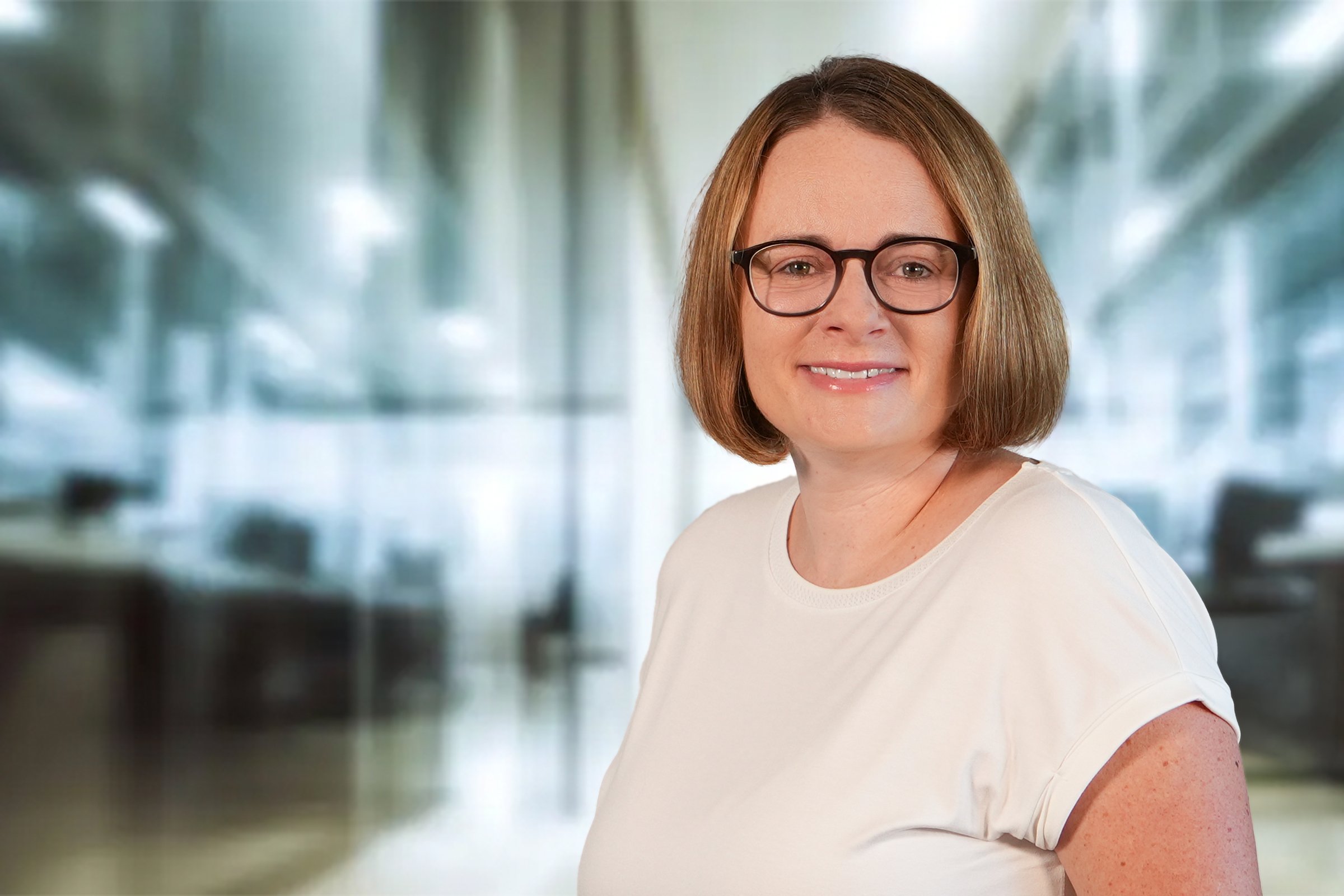 Sarah Roser, Frau mit mittelblonden Bob und Brille im cremefarbenen Kurzarmshirt