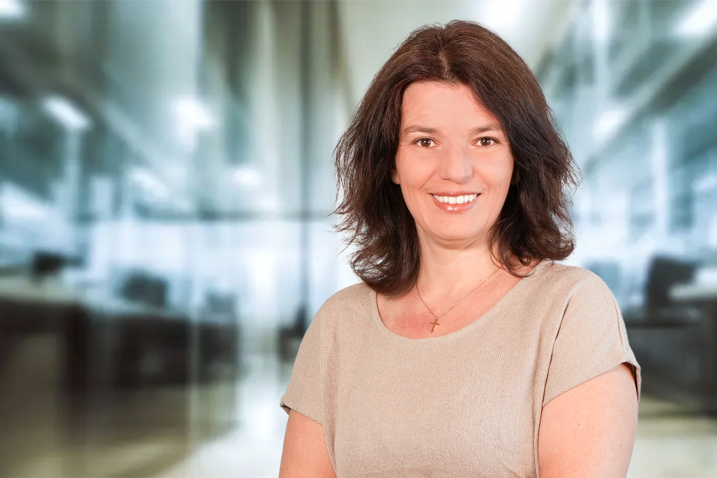 Susan Vetter, Frau mit dunkelbraunen, schulterlagen, gewellten Haaren im beigefarbenen Kurzarm Feinstrickpullover