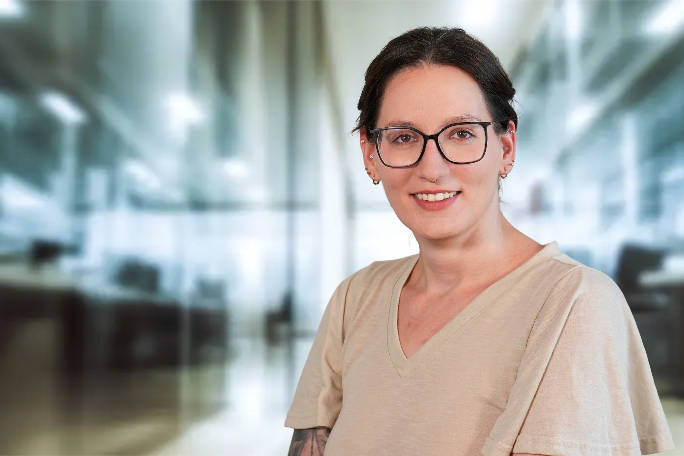 Yvonne Raff, junge Frau mit dunklen, nach hintengebundenen Haaren mit Brille und beigefarbenen V-Ausschnittshirt